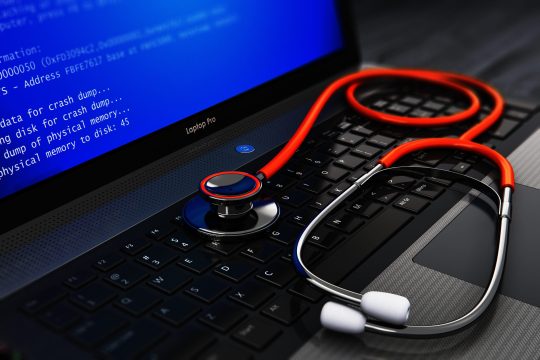 Creative abstract computer bug, virus and service, repair and maintenance technology concept: 3D render illustration of modern black metal glossy business laptop or notebook PC with error message on blue screen BSOD and red medical stethoscope on keyboard on wooden office table with selective focus effect